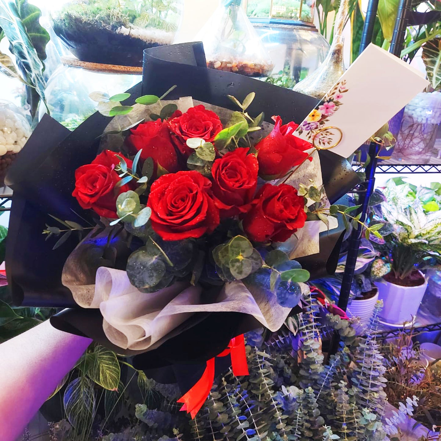 Stunning bouquet of 7 red roses with green leaves, wrapped in decorative paper and tied with a red ribbon, perfect for gifting in Dubai